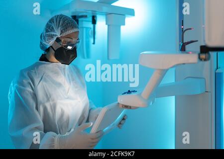 Professional female doctor in medical uniform and protective mask with goggles while using modern diagnostic equipment in hospital Stock Photo