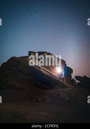 anonymous tourist standing with illuminated torch on stone in mountains on background of starry sky at night Stock Photo