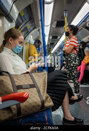 Passengers on the London Underground train carriage wearing face covering and trying to practice social distancing. Stock Photo