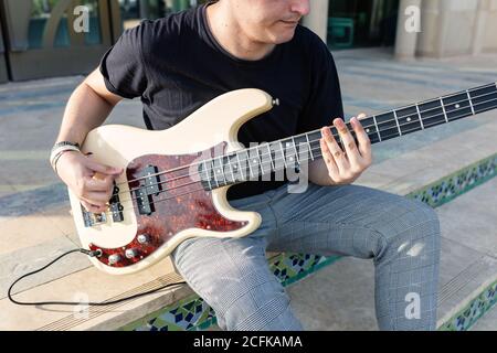 Focused young male musician sitting on floor and performing music on bass guitar Stock Photo