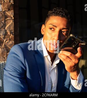 Young successful well dressed black businessman in elegant suit sitting in chair and having pleasant conversation on mobile phone Stock Photo