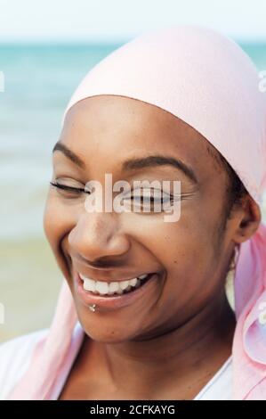 Determined ethnic female with headdress and piercing standing on beach on background of sea and looking at camera Stock Photo