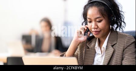 Panorama Young adult friendly confidence operator Mixed race of African asian woman with headsets working in a call center with her colleague in backg Stock Photo