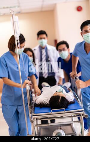 Seriously injured patient with oxygen mask on gurney stretcher bed pushed by medical team of doctor nurse and paramedic to the Operating Room. Emergen Stock Photo