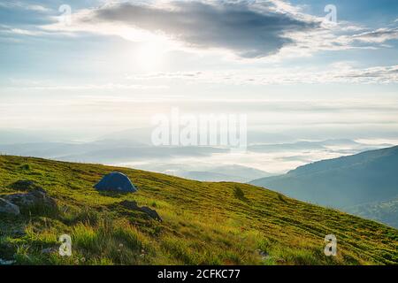 Lonely tourist tent high in the mountains with beautiful panoramic view on the morning foggy valley Stock Photo
