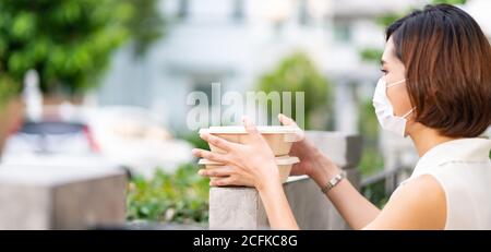 Panorama asian woman with face mask customer take food boxes from the fence post that delivery man put them on for contactless food delivery. This can Stock Photo