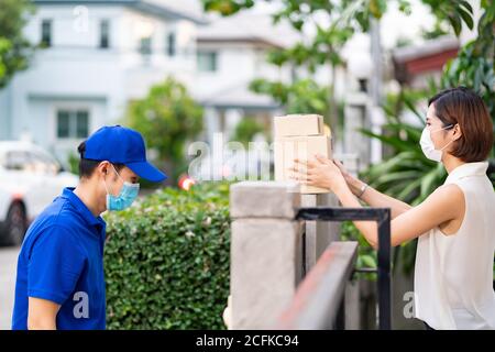 Side view asian woman with face mask customer take shopping packages from the fence post that delivery man put them on for contactless delivery. This Stock Photo