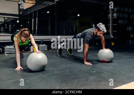 Full length of strong determined athletic man and Woman doing plank exercise using one hand with medicine ball during workout in gym Stock Photo