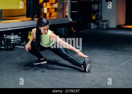 Full body female athlete in sportswear doing stretching exercise while training in modern gym Stock Photo
