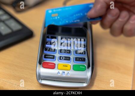 A customer making a contactless card payment on a card reader in a retail shop. Stock Photo