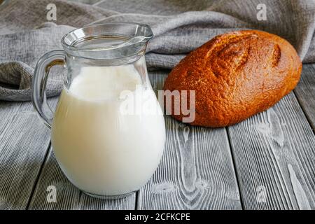 Simple food on the table, milk in a jug, and freshly baked crusty bread. Rustic table made of planks. Canvas fabric Stock Photo