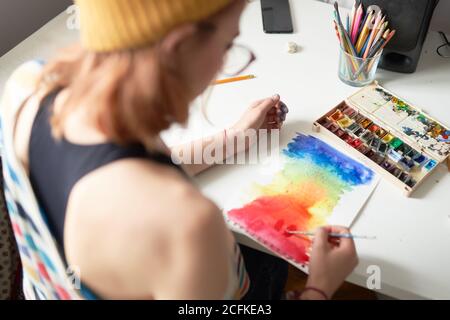 High angle back view of anonymous crop female painter creating aquarelle picture of color spectrum in workshop Stock Photo