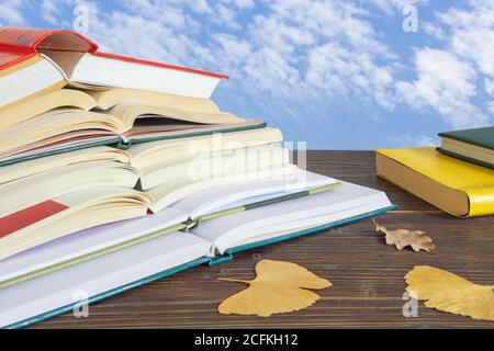 Autumn. Stack of open books and yellow leaves  on the table against blue sky Stock Photo
