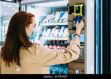 woman with a face mask uses her credit card to pay at the vending machine Stock Photo