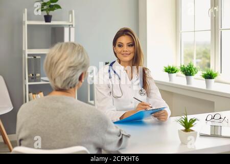 Smiling woman doctor listening to senior woman patient and making notes in medical clinic Stock Photo