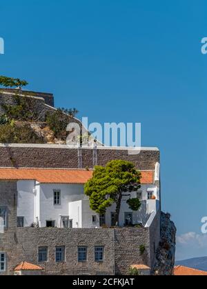 Close to the Edge. A historical building with white-washed and stone walls lies under the clear blue sky and over the steep rocky cliff on the right. Stock Photo