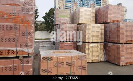 Red perforated bricks with rectangular holes on wooden pallets in an open-air warehouse ready for sale. New bricks on pallets at a hardware store Stock Photo