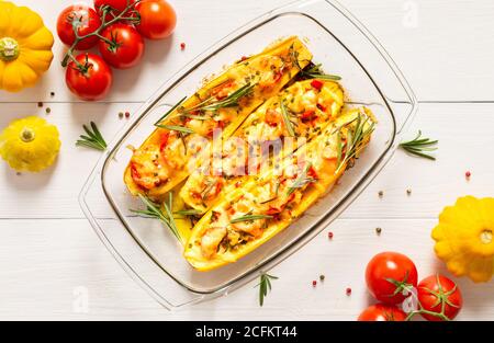 Stewed yellow zucchini with tomatoes and onions, cheese and herbs, carrots and spices, stuffed zucchini on a white wooden background Stock Photo