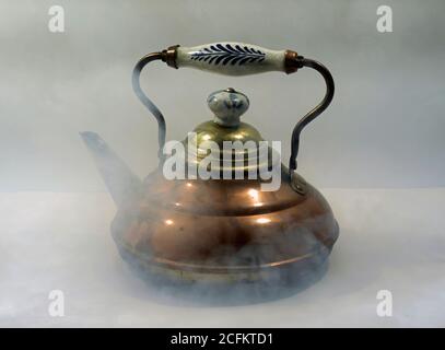 Old often repaired copper kettle. The blue white grip indicates a Dutch origin. There is steam around the kettle. Stock Photo