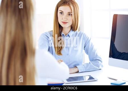 Business woman portrait while shaking hands with her female colleague or clientn in sunny office. Casual clothes style of business people. Audit, tax Stock Photo