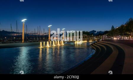 Beautiful night view of fountains, streetlamps at port of Ouchy, Lausanne, Switzerland. Landscape and reflection in water. Stock Photo