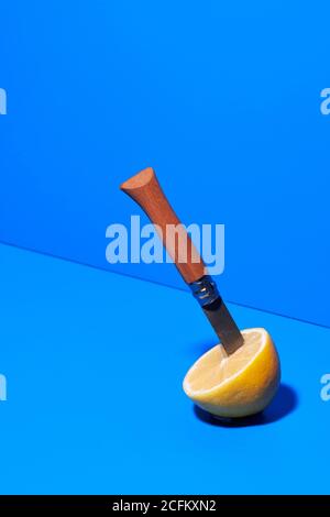 Half of ripe lemon with sharp knife placed on blue background in studio Stock Photo
