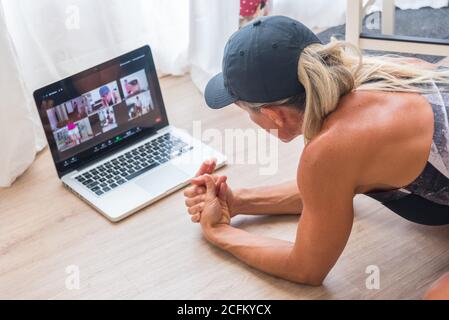 From above back view of fit female athlete in sportswear watching video online on laptop before home workout Stock Photo