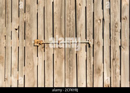 Weathered wooden door with rusty metal bolt on sunny day in Sa Caleta Stock Photo