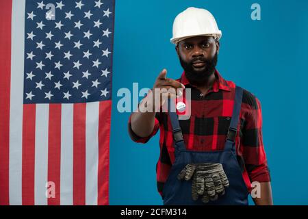 Builder of African ethnicity in hardhat, overalls and flannel pointing at you Stock Photo
