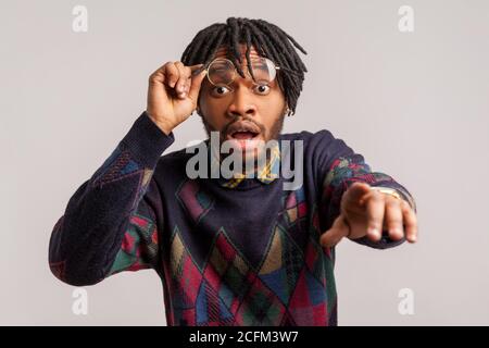 Closeup surprised shocked african man with dreadlocks putting off glasses looking with big eyes and pointing finger at camera, suspecting you. Indoor Stock Photo