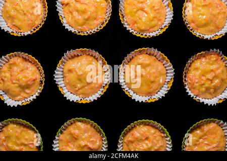 The process of making carrot muffins. Dough for cakes in paper molds on a black background. Selective focus, top view. Stock Photo