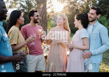 Large group of young happy multicultural friends with drinks standing in circle Stock Photo