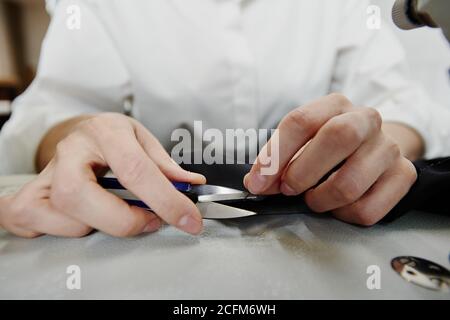 Hands of young contemporary seamstress or female tailor cutting black thread Stock Photo