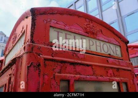 Old red telephone booth with rust and stripped paint. Stock Photo