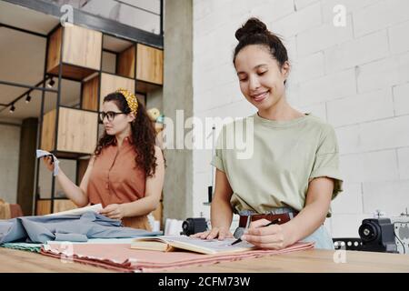 Happy young fashion designer pointing at sketch for new seasonal collection Stock Photo