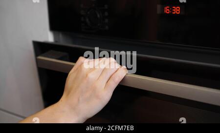 Close up of women hand opening the oven door to control the roast. Young woman cooking in the kitchen opening the oven door Stock Photo