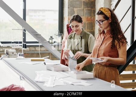 Contemporary young seamstresses in casualwear packing new shoulder pads Stock Photo