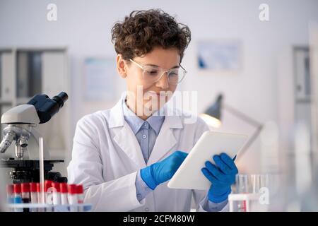 Happy young contemporary female scientist looking through online information Stock Photo