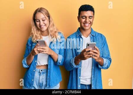 Young interracial couple using smartphone smiling with a happy and cool smile on face. showing teeth. Stock Photo