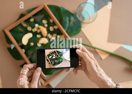 Hands of creative mature woman with smartphone taking photo of composition Stock Photo