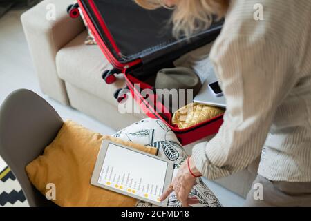 Mature woman pointing at tablet display with list of things to take for journey Stock Photo