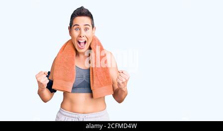Young woman with short hair wearing sportswear and towel using smartphone celebrating surprised and amazed for success with arms raised and open eyes. Stock Photo