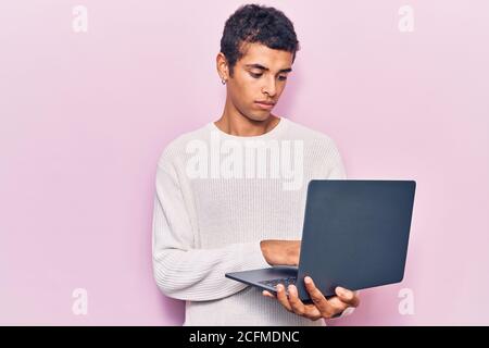 Young african amercian man holding laptop thinking attitude and sober expression looking self confident Stock Photo