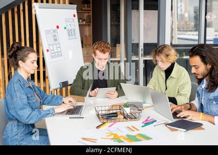 Young contemporary co-workers in casualwear using mobile gadgets in office Stock Photo