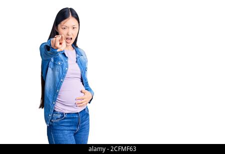 Young beautiful chinese woman pregnant expecting baby pointing displeased and frustrated to the camera, angry and furious with you Stock Photo