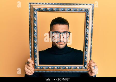 Handsome man with tattoos holding empty frame depressed and worry for distress, crying angry and afraid. sad expression. Stock Photo