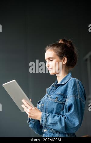 Young brunette female office worker in denim casualwear using digital tablet Stock Photo