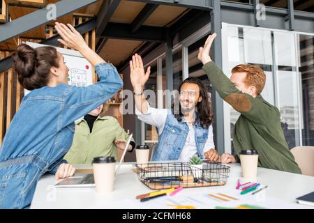 Four young joyful and successful colleagues giving each other high five Stock Photo
