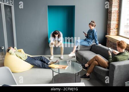 Three young restful designers or developers of mobile applications using gadgets Stock Photo