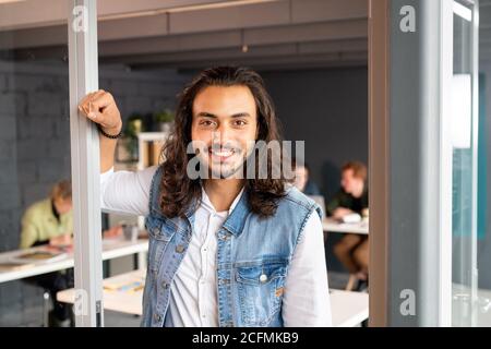 Happy young mixed-race businessman with toothy smile standing by open door Stock Photo